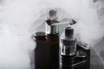 Close view of vaping device with mist on a wooden dark background