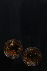 Top view of two glasses of whiskey with ice on a stone table.