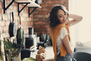 A young, beautiful, charming woman with a sweater on her shoulders posing in the kitchen at home