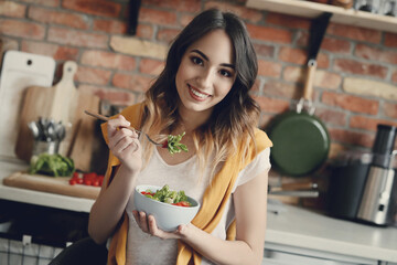 A young, beautiful, charming woman with fresh vegetable salad looking into the camera at the...