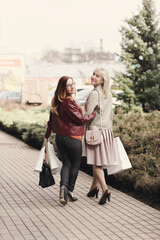 Two middle-aged girlfriends holding shopping bags and walking on the street