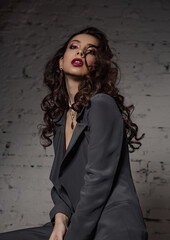 Sexy young makeup beautiful slim model with red lipstick posing in grey style suit clothing  on studio brick background. Closeup