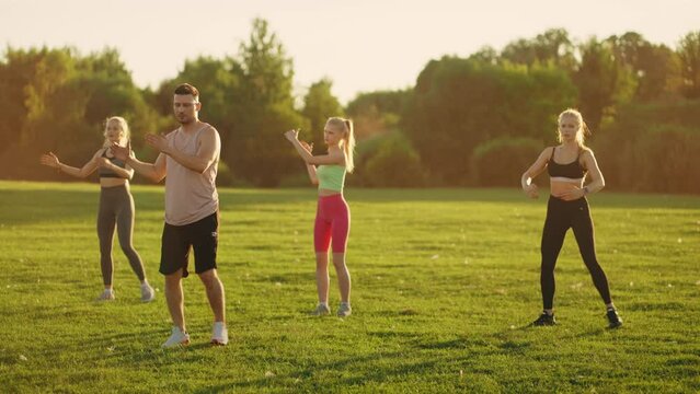 athletic people are exercising outdoors, group fitness class in park, good-looking women are training