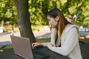 Photo of a young,attractive,Asian woman freelancer sitting at the cafe outdoor and working on the computer