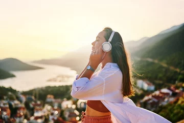 Foto op Plexiglas Inspired happy serene female with closed eyes enjoying of listening calm music with beautiful view at sunset time. Relief stress and healthy minds © Goffkein
