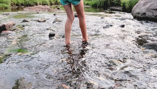 a girl with bare feet walking on a fast river among stones.