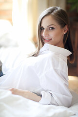 A young, beautiful woman with blond hair in a white shirt posing on a clean bed