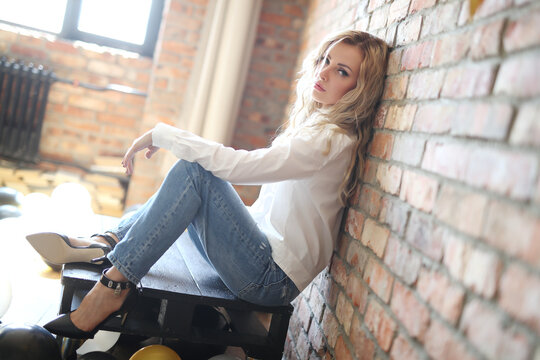 Young, beautiful woman with wavy hair in a white shirt and jeans posing against a stone background