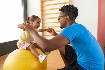Black father and daughter exercising with fit ball 