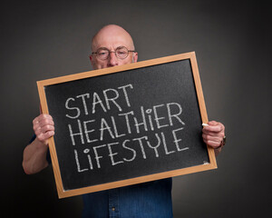 start healthier lifestyle blackboard sign held by a senior man, teacher, mentor or presenter