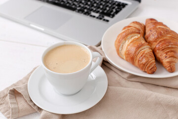 A cup of aroma coffee with croissants and computer on a marble background