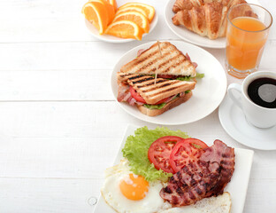 Morning breakfast with fried eggs,bacon,sliced vegetables,croissants and a cup of coffee on a wooden background