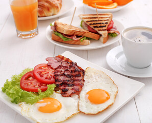 Morning breakfast with fried eggs,bacon,sliced vegetables,croissants and a cup of coffee on a wooden background