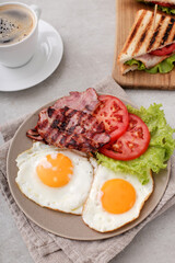 Morning breakfast with fried eggs,bacon,sliced vegetables and a cup of coffee on a marble background