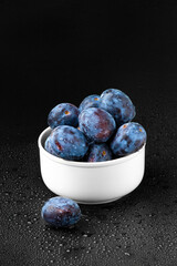 Blue plum in a white plate on a dark background.