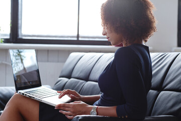 Image of a beautiful woman with curly hair holding office computer and sitting on the sofa