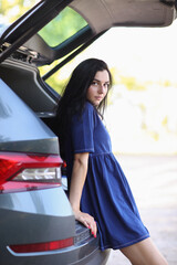 Portrait of a young woman with blue dress sitting at car trunk