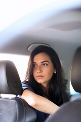 Photo of a young, brunette woman in a blue dress posing for a camera in her car