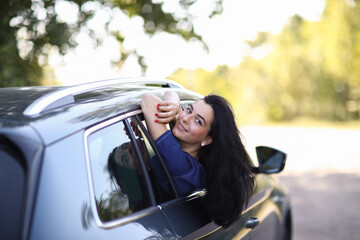 Photo of a young, brunette woman in a blue dress sticking her head outta the windshield of car