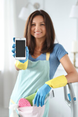 Portrait of middle age woman with cleaning products holding mobile phone at home.