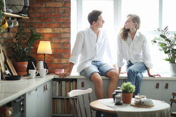 Photosession of beautiful,young couple sitting on the windowsill in the kitchen room