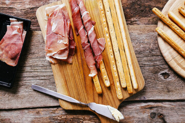 Top view of delicious snacks with bacon and breadsticks isolated on a wooden cutting board.