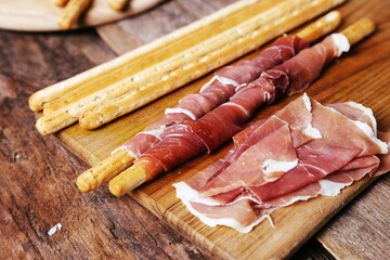 Image of delicious snacks with bacon and breadsticks isolated on a wooden cutting board.