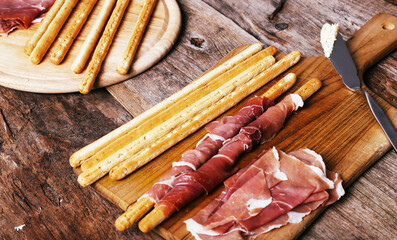 Image of delicious snacks with bacon and breadsticks isolated on a wooden cutting board.