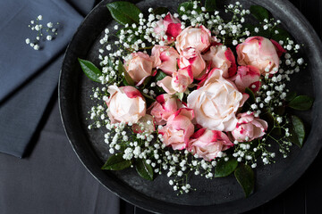 Schöne Rosen mit Schleierkraut dekorativ angeordnet auf dunklem Tablett mit passender Tischware