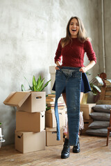 Cute girl in red sweater trying on new jeans against cardboard boxes