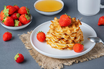 Viennese waffles with strawberries and honey on a gray table