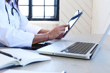 Young, professional, confident female doctor with stethoscope holding a digital tablet at doctor's office