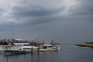 Cape Cod coastal scene. Threatening dark gray storm clouds over boats anchored at dock near...
