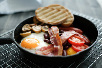 Side view of English breakfast with fried eggs, bacon, mushrooms,bread and vegetables in pan.