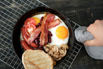Top view of English breakfast with fried eggs, bacon, mushrooms,bread and vegetables in pan.