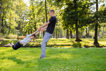 Young father twirling his little son in park.