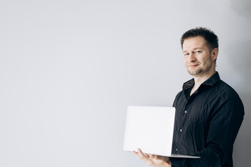 Confident IT specialist in black shirt holding laptop and smiling.