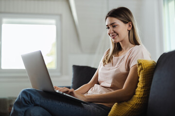 Fototapeta premium Happy young woman using computer on sofa at home