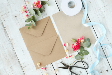 Top view of cardboard envelope with scissors, ribbons and artificial flowers on a wooden background