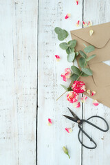 Top view of cardboard envelope with scissors and artificial flowers on a wooden background