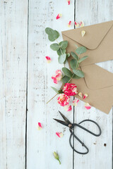 Top view of cardboard envelope with scissors and artificial flowers on a wooden background