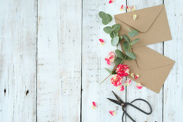 Top view of cardboard envelope with scissors and artificial flowers on a wooden background
