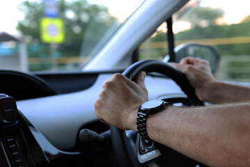 Beautiful male hands with a smart watch holding the steering wheel while driving a car. Safe driving concept