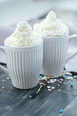 Two white cups of Latte with whipped cream on top on a wooden surface.