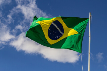 Bandeira do Brasil balançando ao vento com céu e nuvens ao fundo. - obrazy, fototapety, plakaty