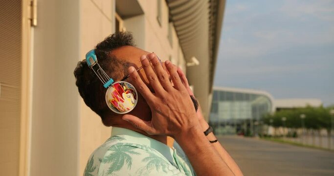 Emotional side portrait of the young happy african man in pink sunglasses and headphones laughing near the airport. 4k footage.