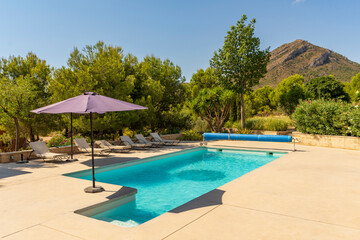 Swimming pool with umbrellas in a country house on a sunny day surrounded by nature and mountains