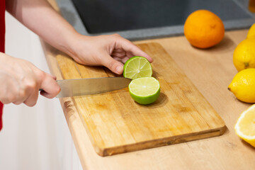 Female hands cut lime on a wooden board in the kitchen. Cooking delicious lemonade. Recipe and cooking tips. making cocktails. Slicing lemon fruit. Vegetarianism and veganism