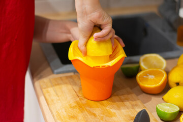Woman squeezes a lemon on the kitchen table oranges, lemons. Step by step cooking delicious cocktails at home. Step: squeezing a lemon. Summer drink. Young woman preparing tasty lemonade in kitchen