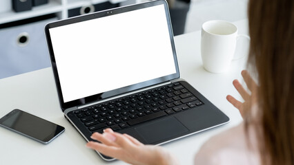 Virtual conference. Female speaker. Digital mockup. Unrecognizable woman talking to laptop with blank screen gesturing hands in light room interior.